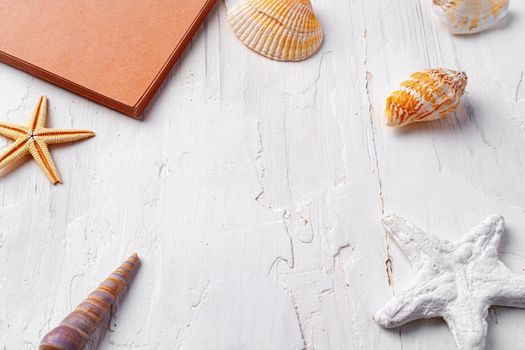 Brown open notepad surrounded by sea shells on white wooden table, copy space
