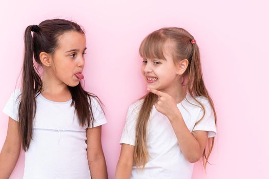 Image of two angry teenage girls with braids in casual clothes standing isolated over pink background