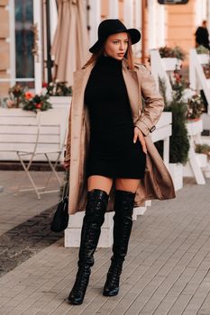 Stylish young woman in a beige coat in a black hat on a city street. Women's street fashion. Autumn clothing.Urban style.