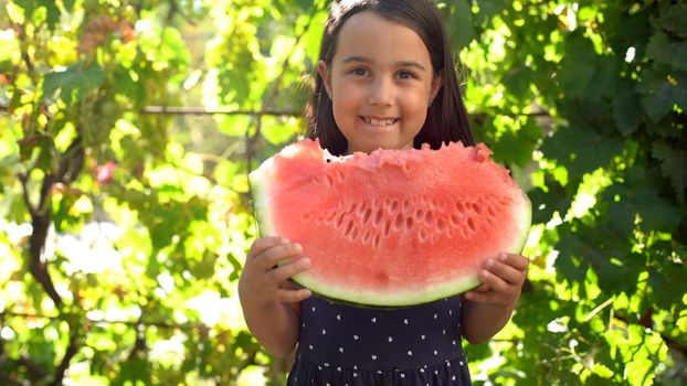 Happy child eating watermelon. Kid eat fruit outdoors. Little girl playing in the garden biting a slice of watermelon.