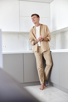 Happy handsome man is standing on minimalistic kitchen and smiling