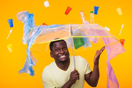 Plastic recycling problem, ecology and environmental disaster concept - Surprised african american man on yellow background with trash. He's worried about ecology disaster