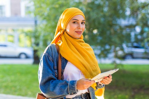 Arab woman student. Beautiful muslim female student wearing yellow hijab holding tablet