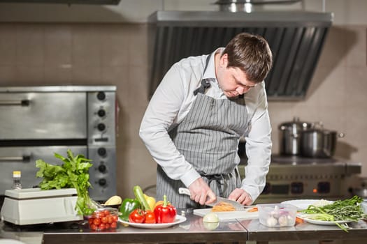 Closeup of hand with knife cutting fresh vegetable. Young chef cutting beet on a white cutting board closeup. Cooking in a restaurant kitchen.