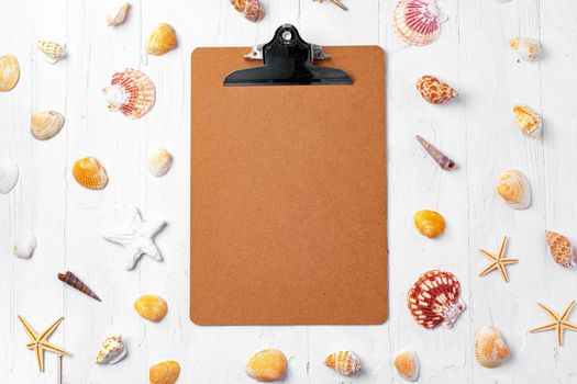 Clipboard with sea shells on white wooden table close up, copy space.