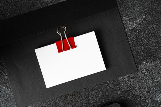 White businesscards united with a paper clip on a black rough background, copy space