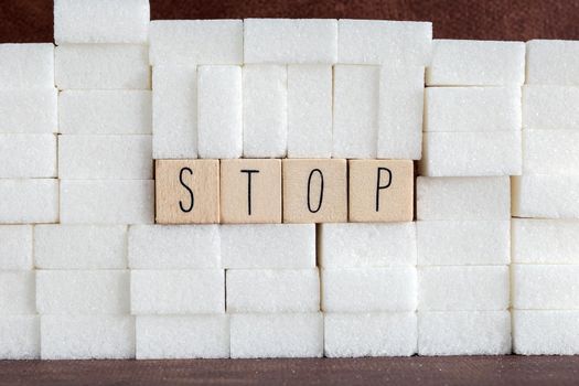 Pile or wall of sugar cubes and stop word in block letters as advise on addiction calories excess and sweet unhealthy food abuse causing health problem and overweight background concept.