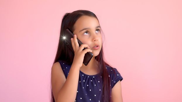 Little preschooler girl in a dress holding a mobile phone, isolated over pink