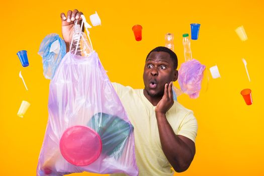 Problem of trash, plastic recycling, pollution and environmental concept - surprised man carrying garbage bag on yellow background.