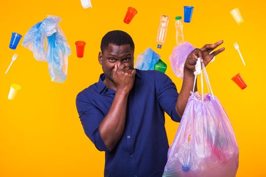 Environmental pollution, plastic recycling problem and waste disposal concept - angry man holding garbage bag on yellow background. He is feel smell of trash.