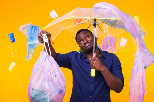 Problem of trash, plastic recycling, pollution and environmental concept - confused man carrying garbage bag on yellow background.