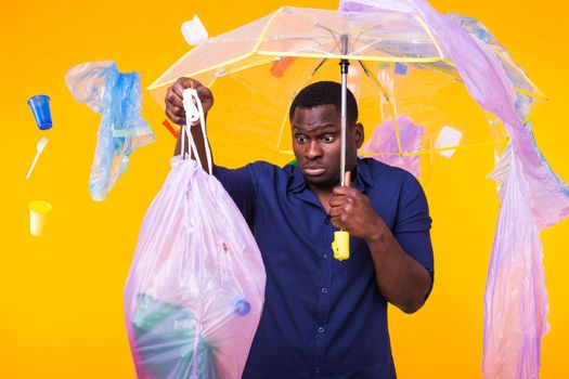 Plastic recycling problem, ecology and environmental disaster concept - Surprised african american man on yellow background with trash. He's worried about ecology disaster