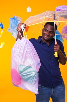 Problem of trash, plastic recycling, pollution and environmental concept - confused man carrying garbage bag on yellow background.