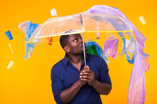 World Environment Day, plastic recycling problem and environmental disaster concept - Surprised african american man looking on trash on yellow.