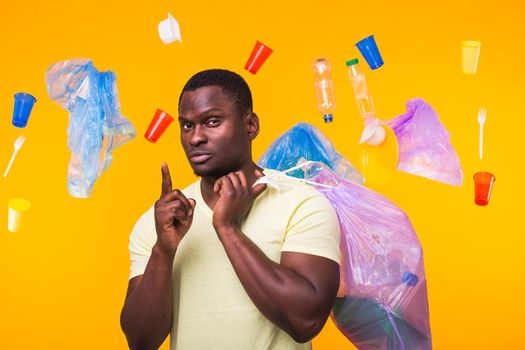 Problem of trash, plastic recycling, pollution and environmental concept - african american man carrying garbage for recycling and pointing up on yellow.