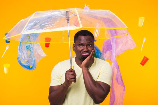 Problem of trash, plastic recycling, pollution and environmental concept - pensive african american man on yellow background with garbage