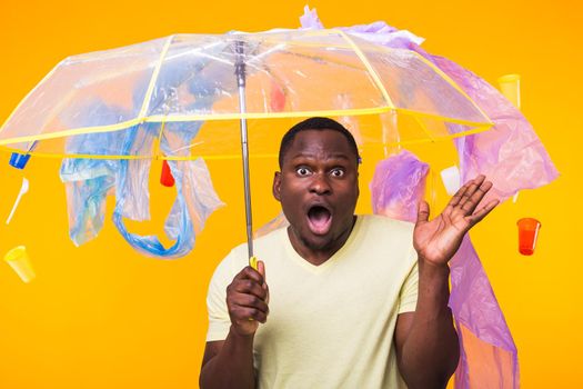 Plastic recycling problem, ecology and environmental disaster concept - Surprised african american man on yellow background with trash. He's worried about ecology disaster