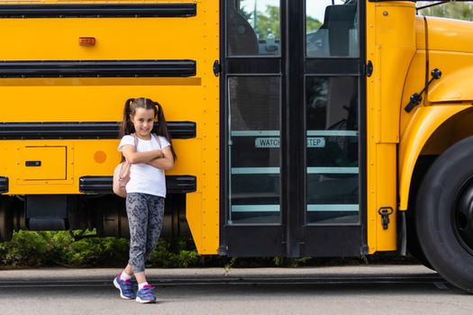 Girl with backpack near yellow school bus. Transport for students