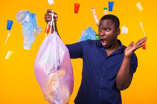 Problem of trash, plastic recycling, pollution and environmental concept - surprised man carrying garbage bag on yellow background.