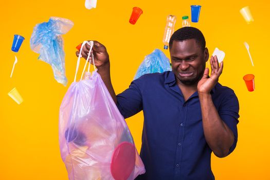 Environmental pollution, plastic recycling problem and waste disposal concept - angry man holding garbage bag on yellow background. He is feel smell of trash.