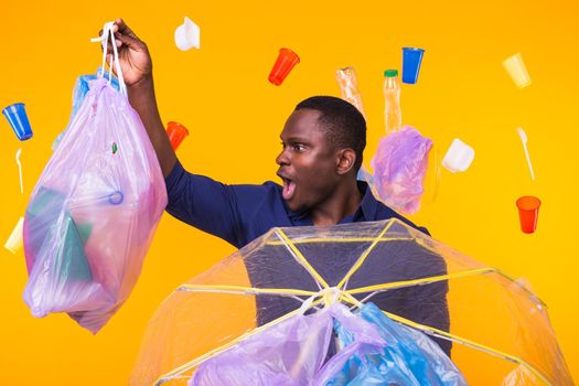 Problem of trash, plastic recycling, pollution and environmental concept - surprised man carrying garbage bag on yellow background.