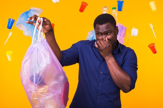 Environmental pollution, plastic recycling problem and waste disposal concept - angry man holding garbage bag on yellow background. He is feel smell of trash.