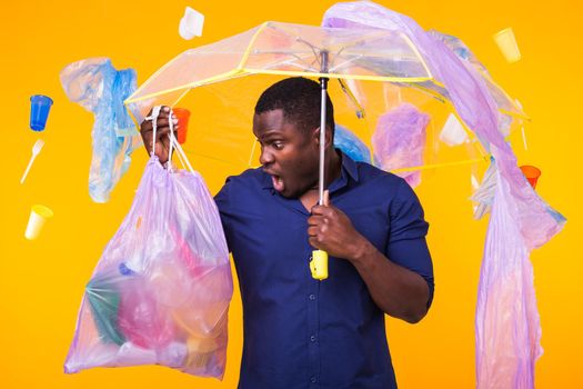 Problem of trash, plastic recycling, pollution and environmental concept - surprised man carrying garbage bag on yellow background.