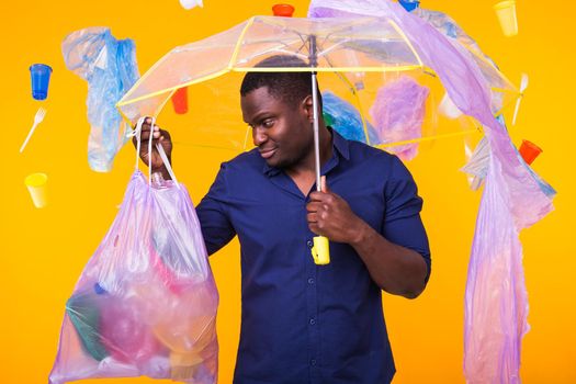 Problem of trash, plastic recycling, pollution and environmental concept - confused man carrying garbage bag on yellow background.