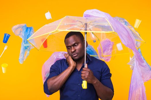 Problem of trash, plastic recycling, pollution and environmental concept - pensive african american man on yellow background with garbage