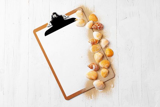 Clipboard with sea shells on white wooden table close up, copy space.