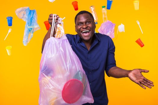 Problem of trash, plastic recycling, pollution and environmental concept - confused man carrying garbage bag on yellow background.