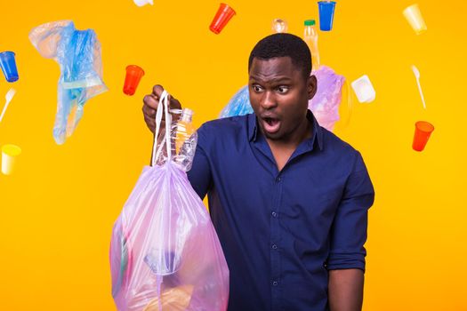 Problem of trash, plastic recycling, pollution and environmental concept - surprised man carrying garbage bag on yellow background.