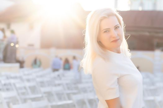 attractive woman dressed in white dress in summer open air theater on chair alone, spring street style fashion trend, social distancing