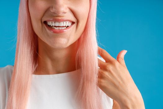 Close up shot of happy young woman with pink hair smiling at camera, posing isolated over blue studio background. Emotions, lifestyle concept