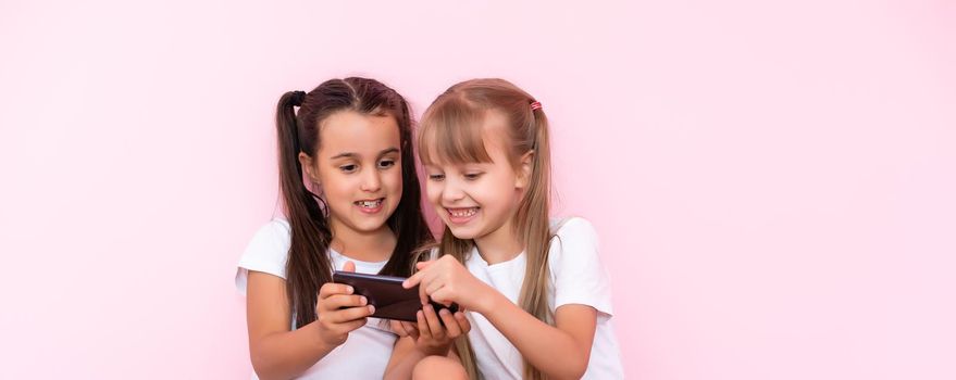 two little girls with a smartphone on a pink background