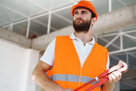 Young male plumber in workwear holding pipe wrench on a construction site indoors