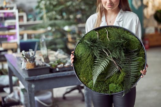 Confident female florist is holding a plant composition in her own flower and plants shop