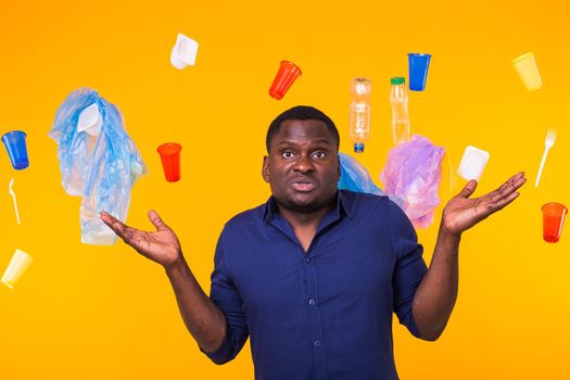 Problem of trash, plastic recycling, pollution and environmental concept - pensive african american man on yellow background with garbage