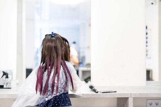 hairdresser dyes hair for a little girl in a hair salon. Dyed, bleached hair