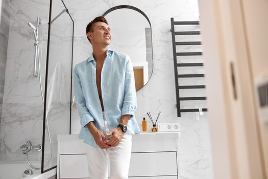 Photo of adult caucasian beautiful man in front of mirror in light modern bathroom