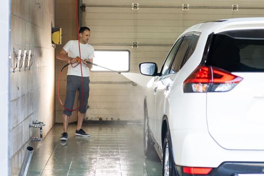 Young tall man spalshing his car by garden hose