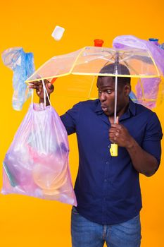 Problem of trash, plastic recycling, pollution and environmental concept - surprised african american man carrying garbage for recycling on yellow