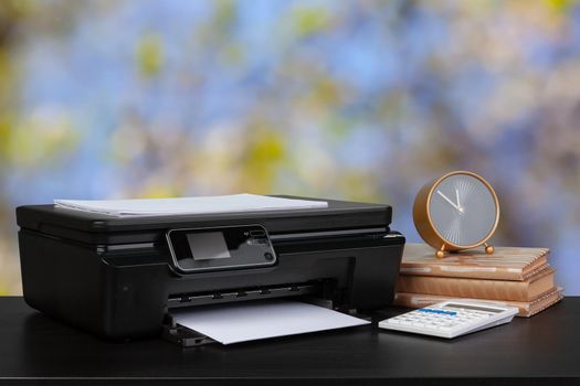 Compact home printer on desk with books against blurred background, close up