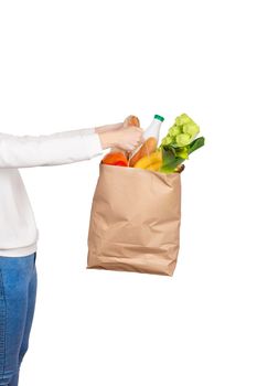 Food delivery or donation concept. Grocery store shoping. Girl holds a paper bag filled with groceries such as fruits, vegetables, milk, yogurt, eggs isolated on white.