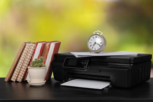 Stack of books and home printer against blurred background, close up