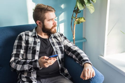 Technologies and leisure concept - Handsome man using smartphone sitting at home