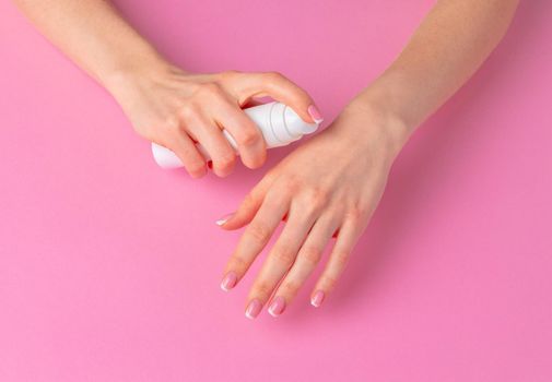 Female hand holding skincare product bottle on pink background