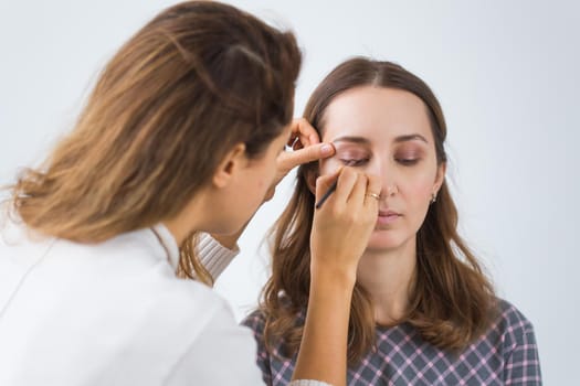 Beauty and cosmetics concept - Makeup artist doing professional make up of young woman.