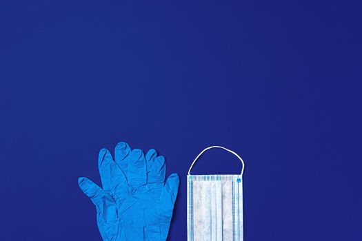 Medical gloves and surgical protective face mask on dark blue background. Coronavirus concept