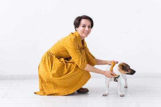 Cheerful young woman posing in a yellow dress with her beloved dog Jack Russell Terrier standing on a white background. The concept of casual wear